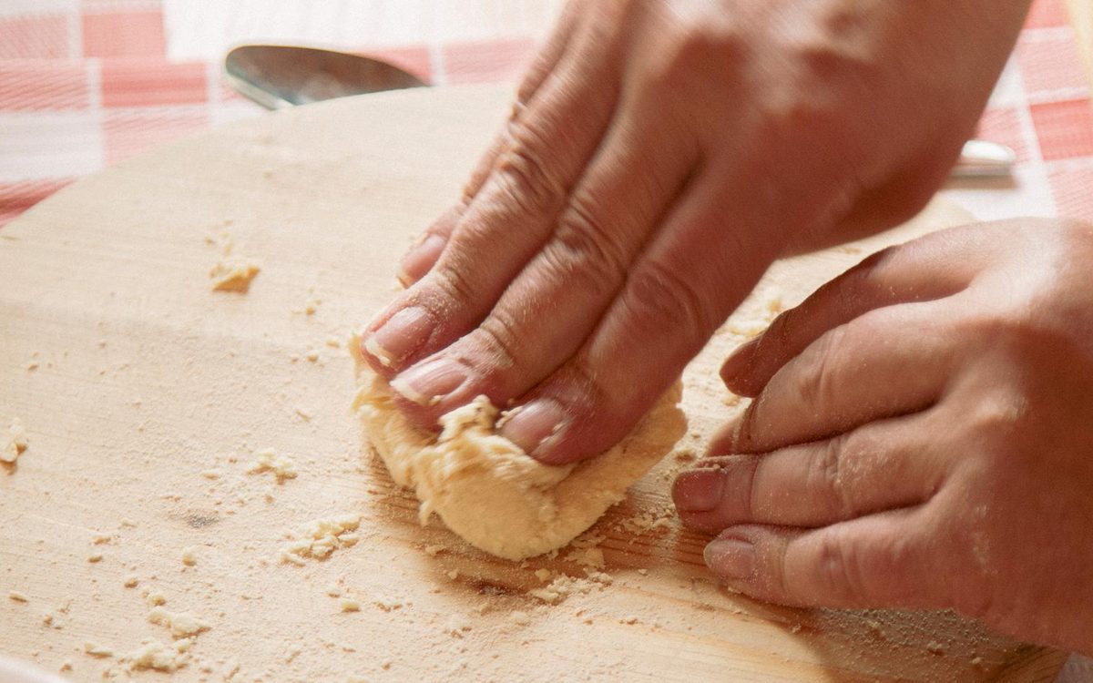 Mani che impastano la pasta fresca su un tagliere di legno