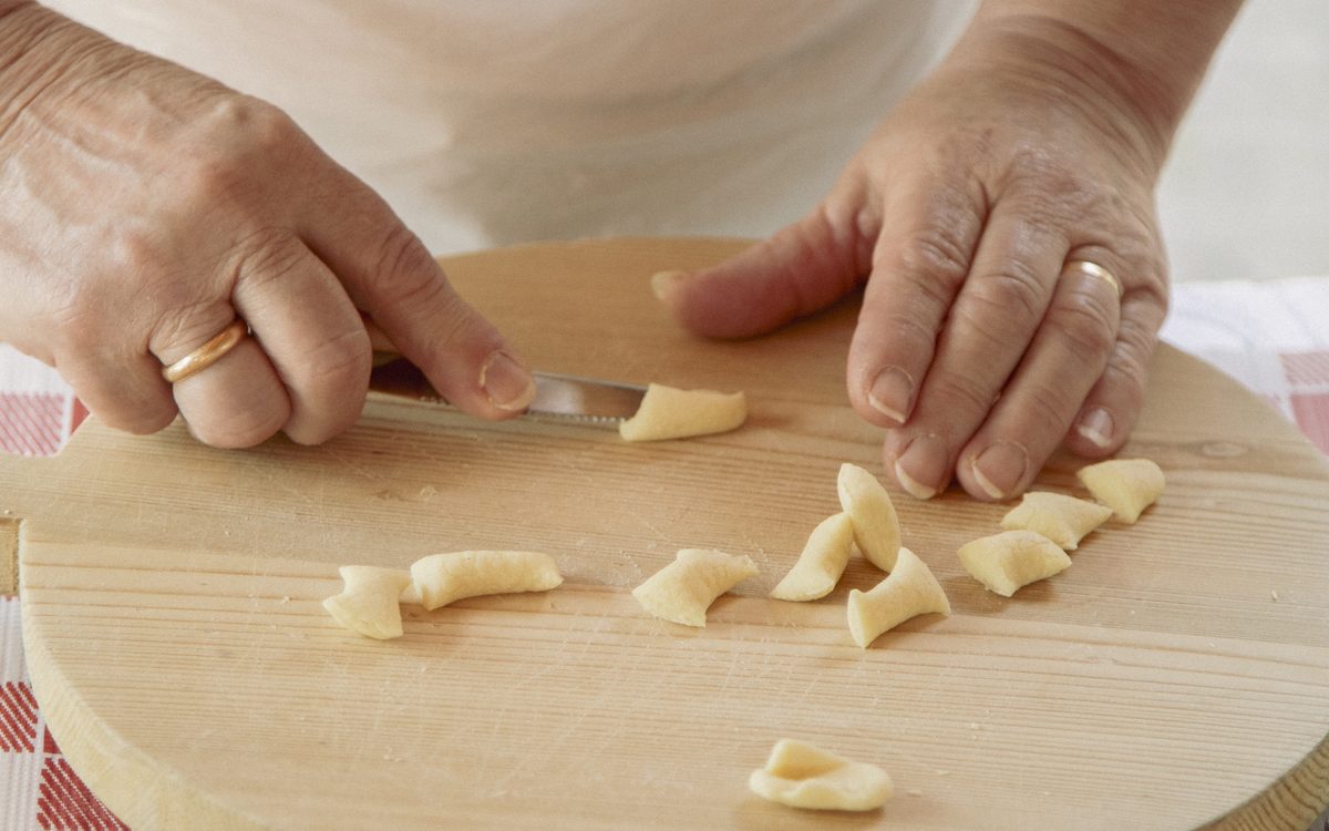 Mani che preparano pasta fresca fatta a mano su un tagliere di legno